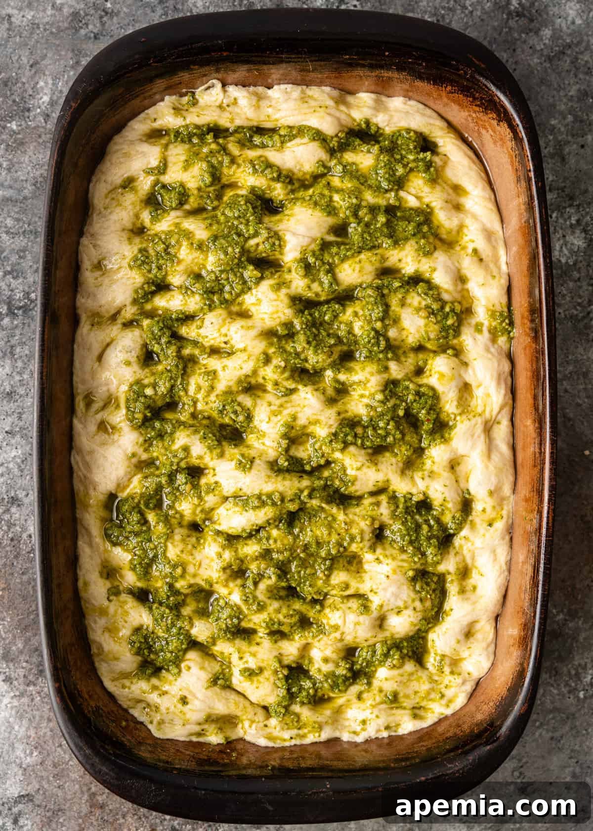overhead process shot: focaccia bread dough in pan after poked and pesto added