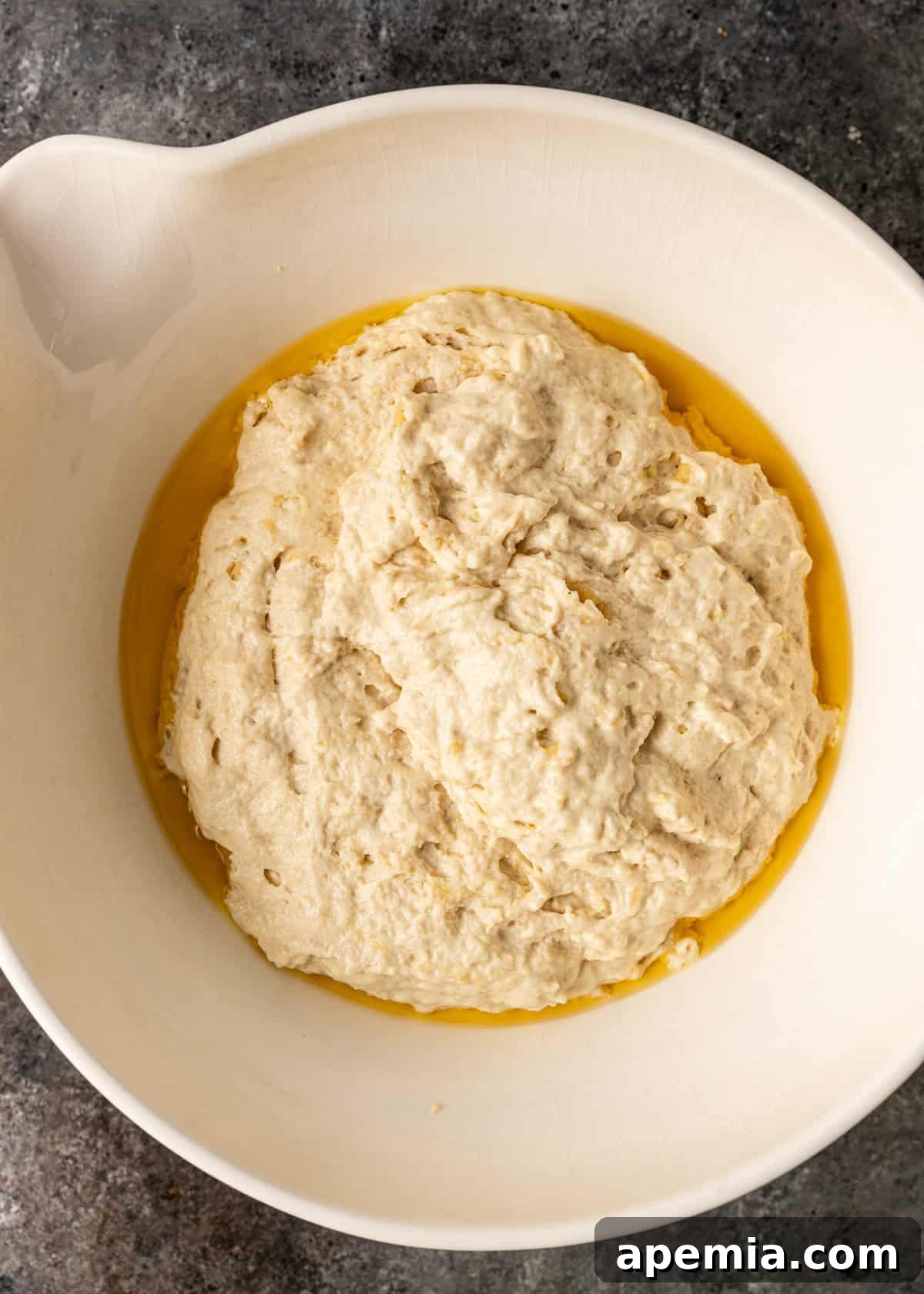 overhead process shot: focaccia bread dough rising in a bowl with olive oil