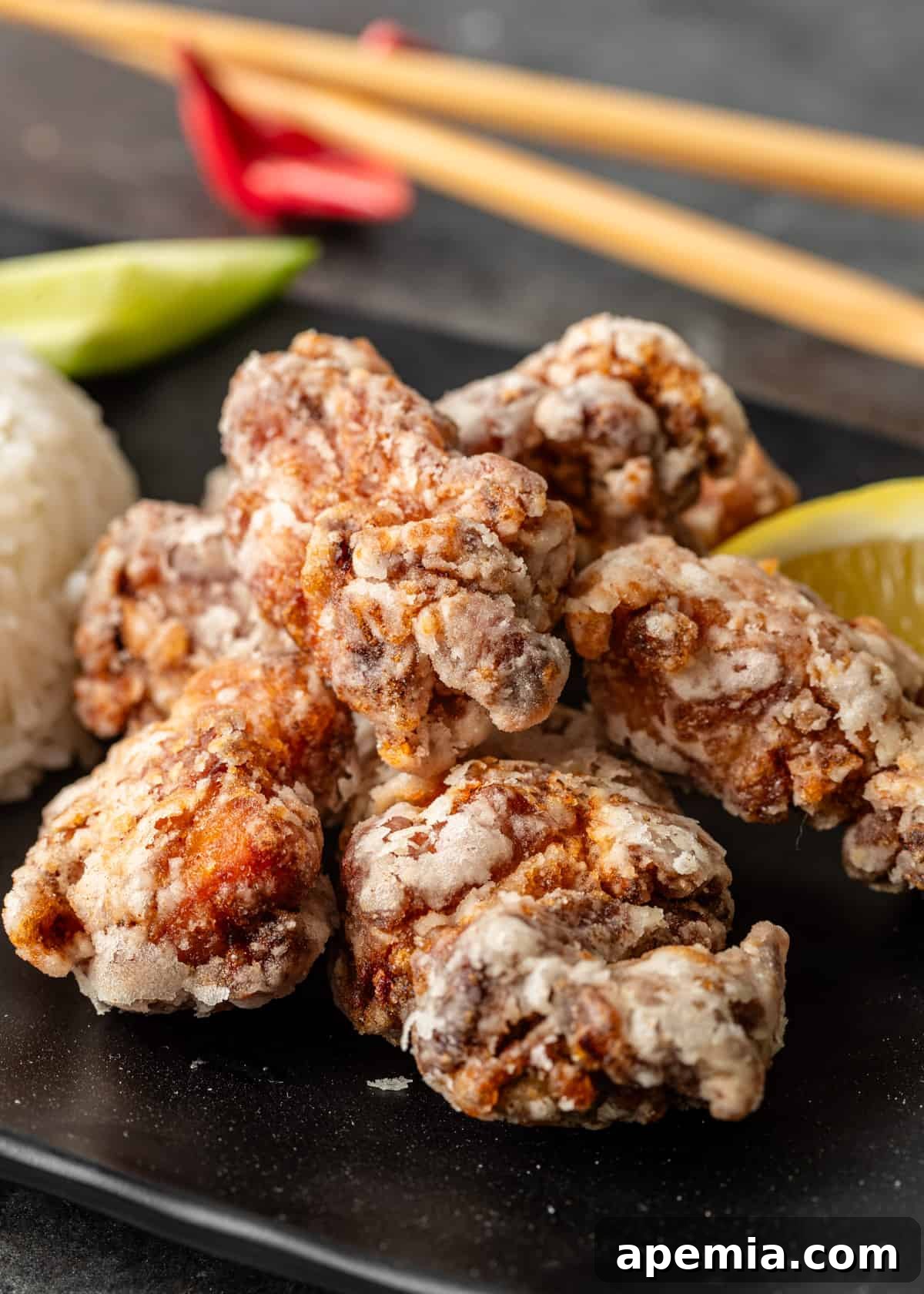 closeup: chicken karaage on a black plate with rice and a lemon wedge to the side