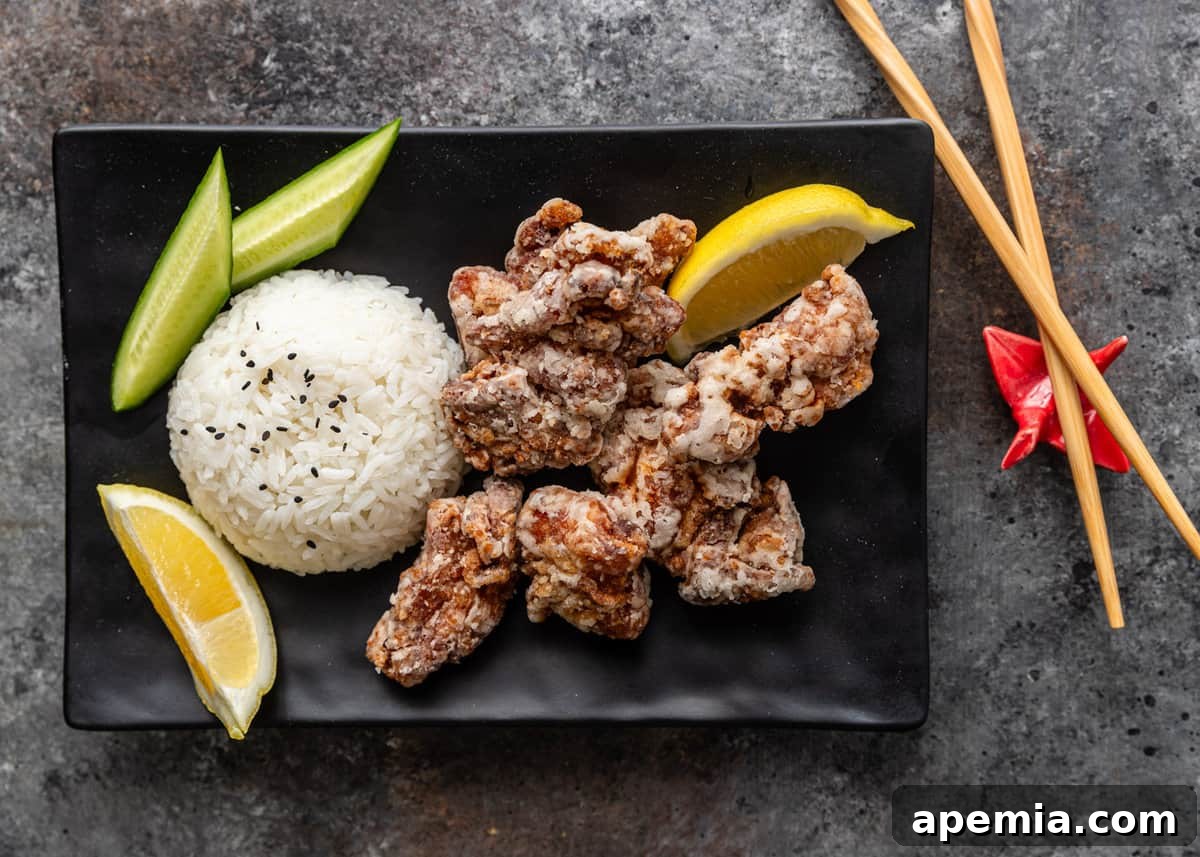 overhead: karaage on a black plate with lemon wedges, rice, and cucumber with chop sticks to the side