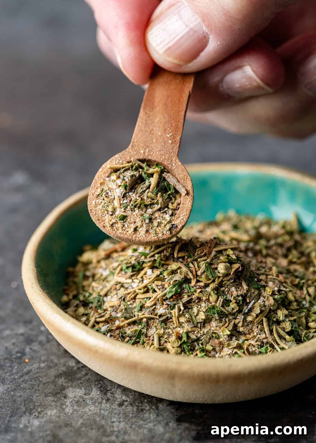 An extreme close-up shot of a hand gently holding a small wooden spoon overflowing with the vibrant homemade Greek seasoning, showcasing its finely ground texture.