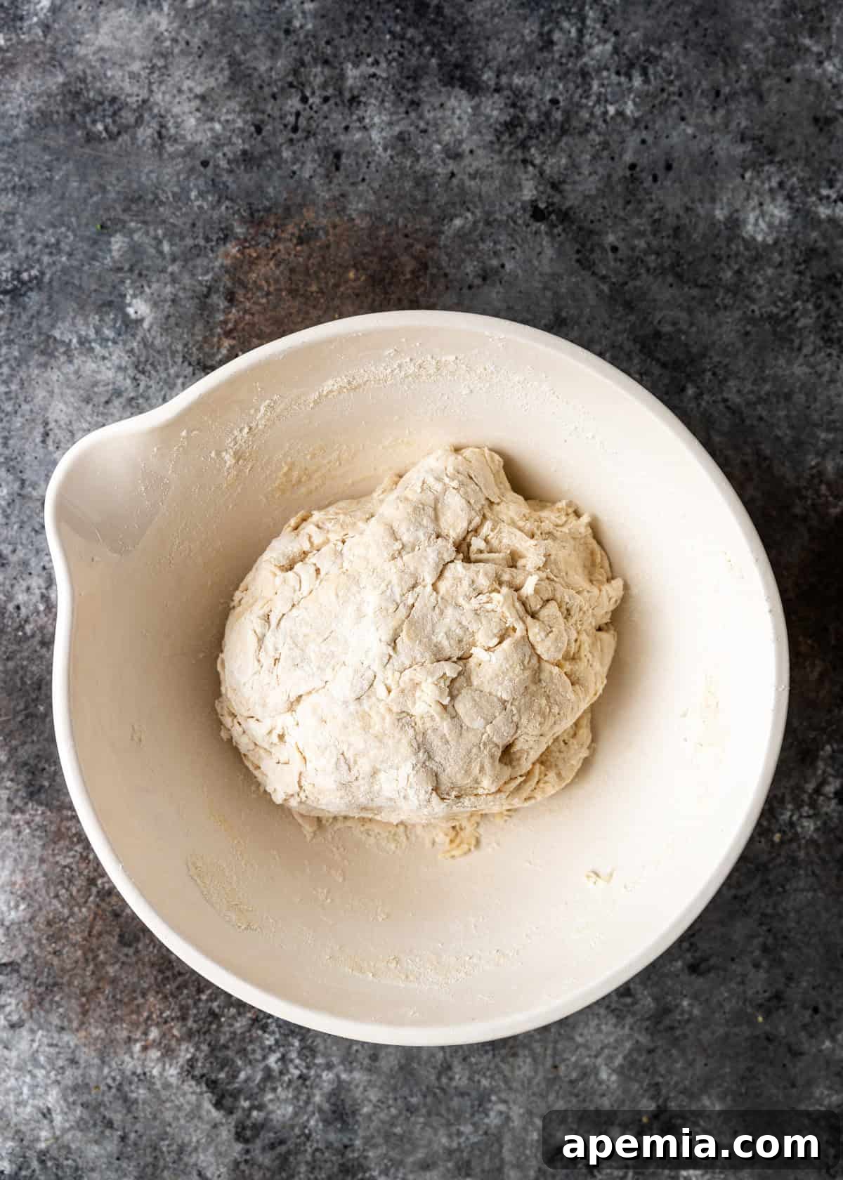 Overhead process shot: Shaggy bazlama dough forming in a large mixing bowl after initial combining of wet and dry ingredients, indicating it's ready for kneading.