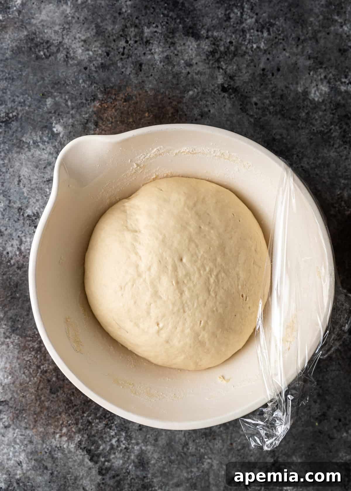 Overhead process shot: Risen bazlama dough in a bowl, visibly doubled in size and light, after resting in a warm environment.