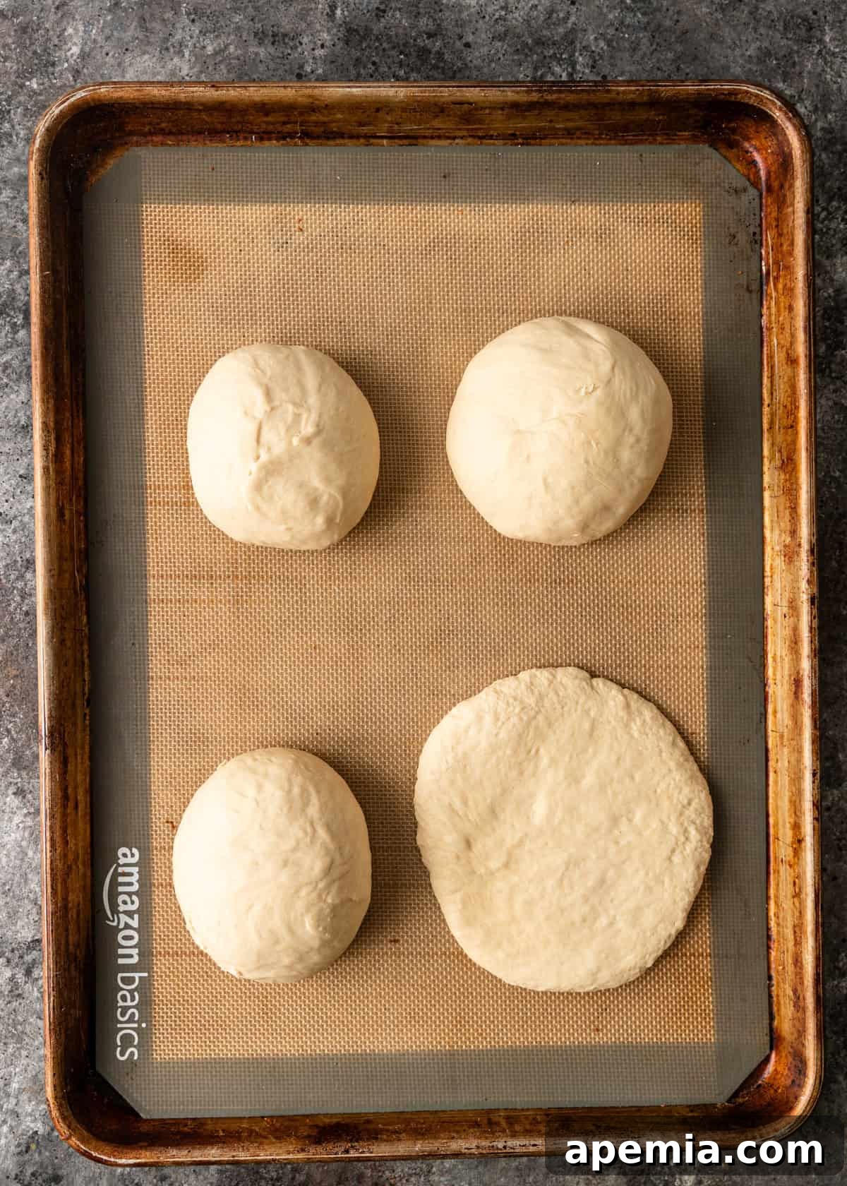 Overhead process shot: Four dough balls with one successfully flattened into a 6-inch circular flatbread shape, illustrating the next stage before cooking.