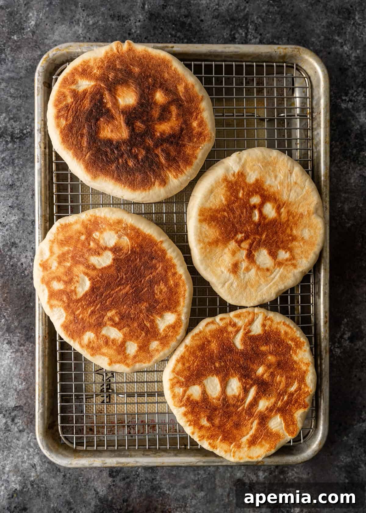 Overhead process shot: Freshly cooked Turkish flatbread (bazlama) cooling on a wire rack over a baking sheet, allowing for proper air circulation.