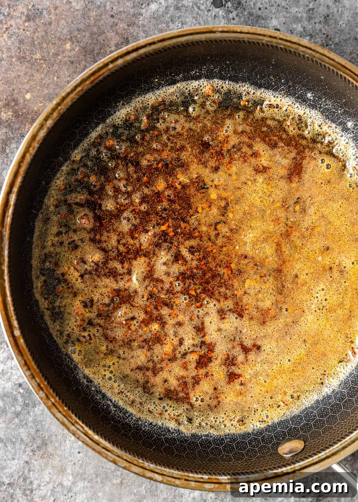 Overhead process shot of butter melting and simmering with red chili flakes in a skillet, creating the aromatic and colorful chili butter for Çilbir.