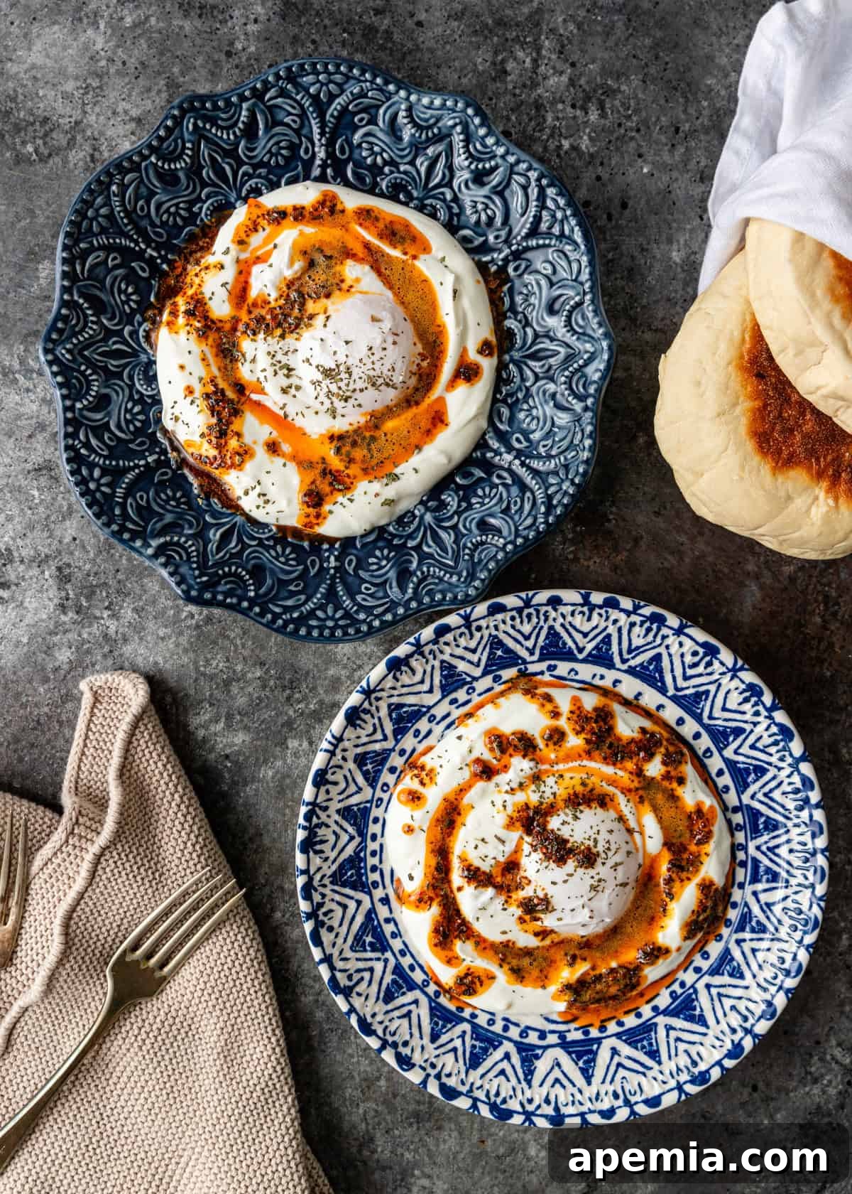 Overhead shot of two blue and white ceramic plates, each holding a serving of Turkish eggs with yogurt, accompanied by a side of fresh flatbread, ready to be enjoyed.