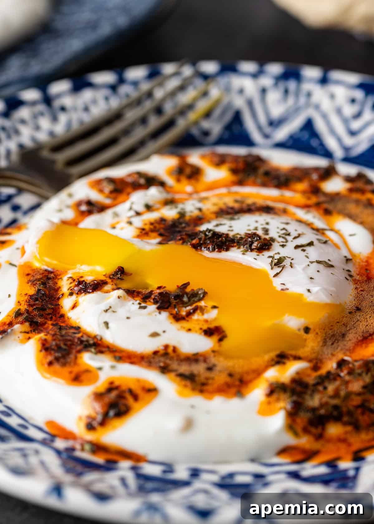 Extreme close-up of a Çilbir serving, showing the glistening runny yolk, rich garlic yogurt sauce, and vibrant chili butter, garnished with fresh mint, ready to be savored.