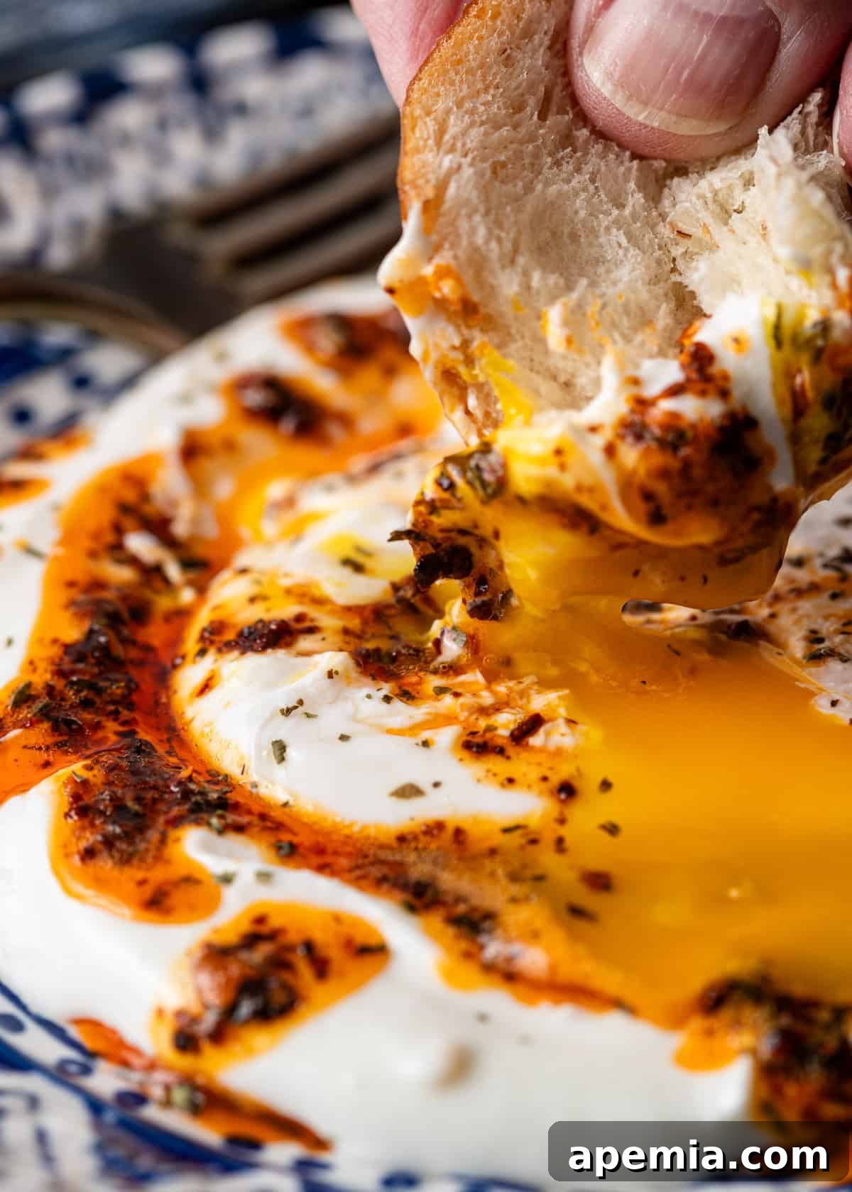 Extreme close-up of Turkish flatbread being dipped into the runny yolk of a Çilbir dish, highlighting the rich textures and inviting flavors, ready for a delicious bite.