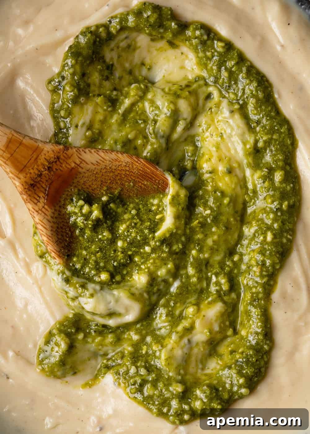 Rich basil pesto mixed into a skillet of creamy alfredo sauce, creating a vibrant green fusion for pasta