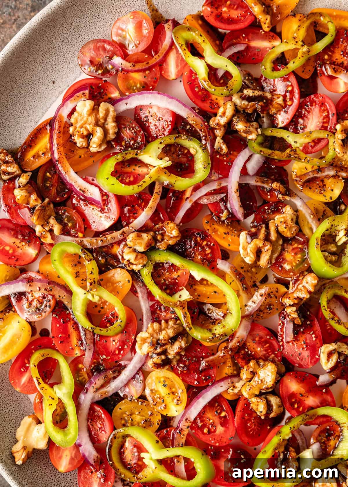 Close-up overhead shot of a prepared Turkish tomato salad with green peppers, red onion, and walnuts, ready to be served.