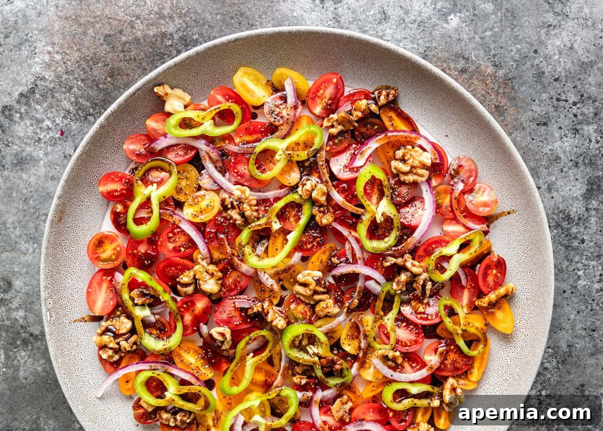 A large white serving platter filled with colorful Turkish Gavurdagi tomato salad, garnished with fresh herbs.