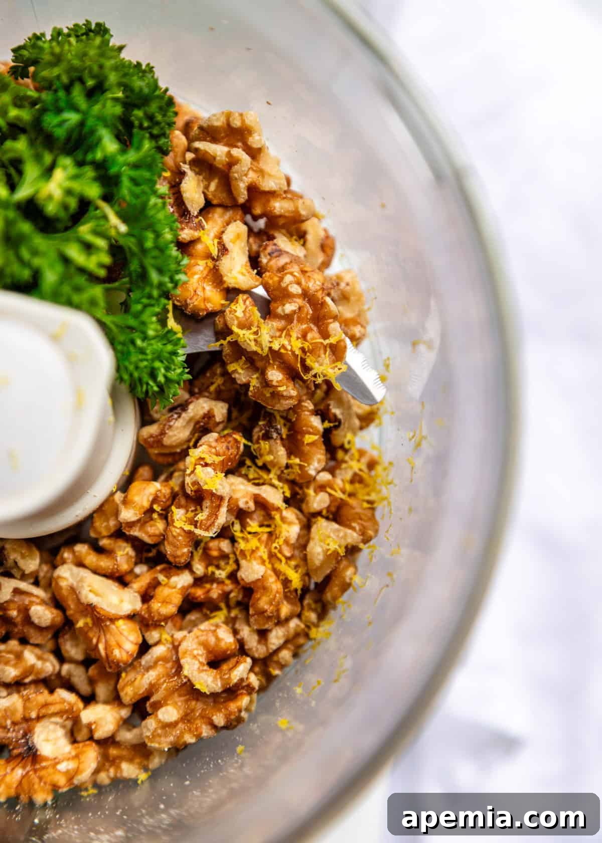 overhead closeup: walnuts, fresh parsley, and bright lemon zest ready in a food processor bowl before blending