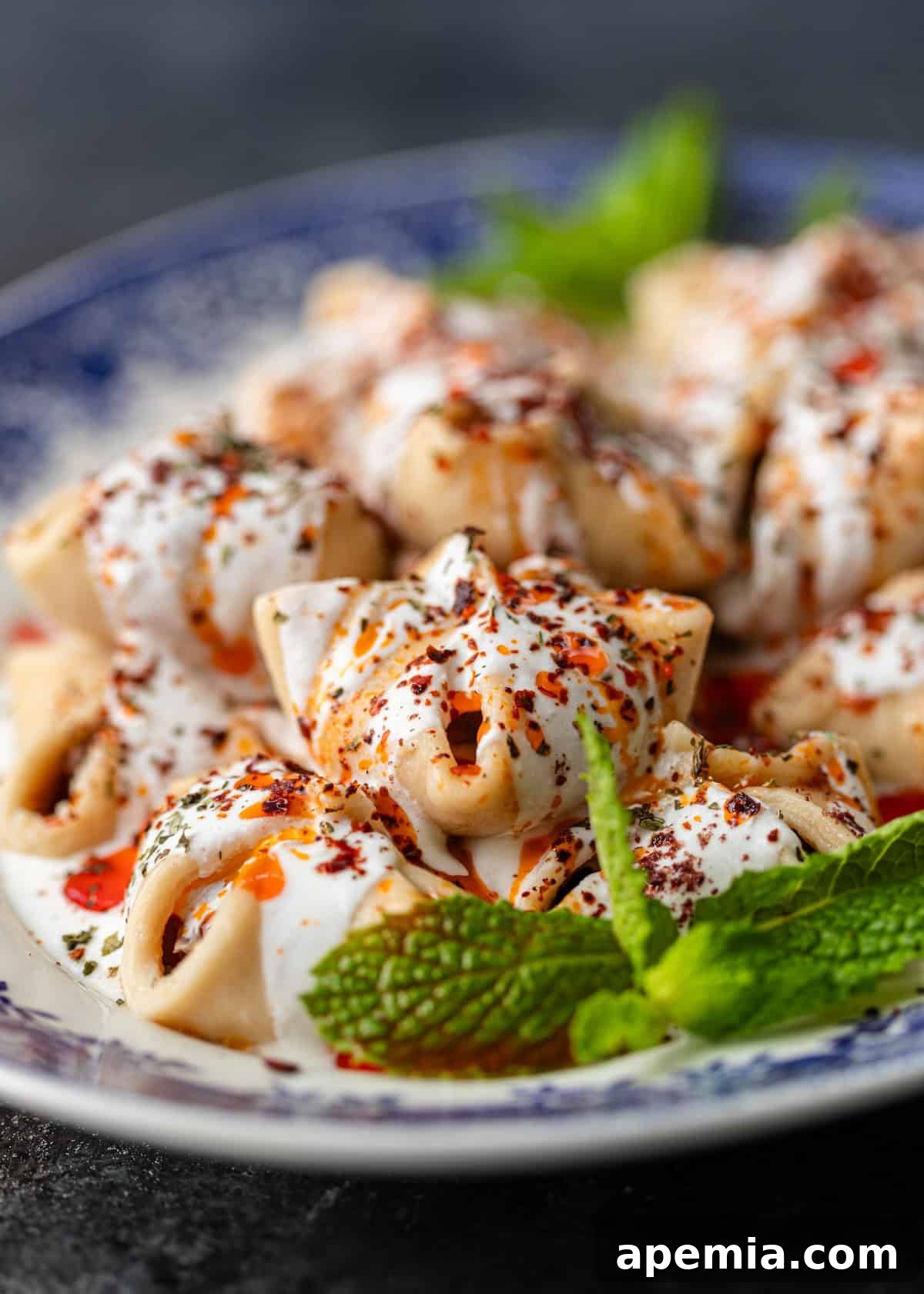 Close-up shot of perfectly cooked Turkish Manti, glistening with a vibrant red chili sauce on top.