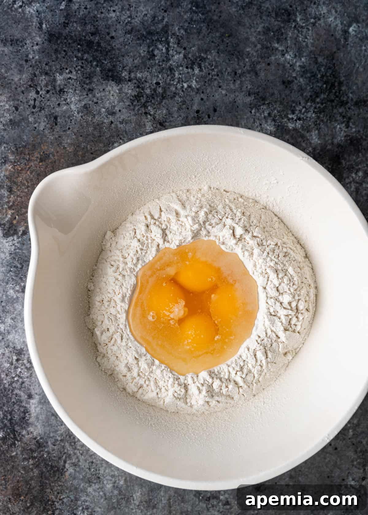 Overhead view of a mixing bowl containing flour and fresh eggs, the base ingredients for Manti dough.