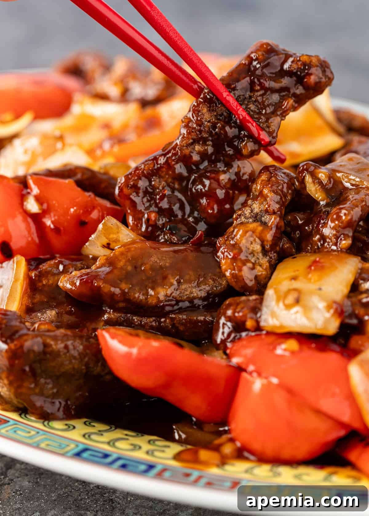 Sweet & Tangy Beijing Beef 3 Close-up shot of red chopsticks lifting a succulent piece of crispy Beijing Beef from the stir-fry mix