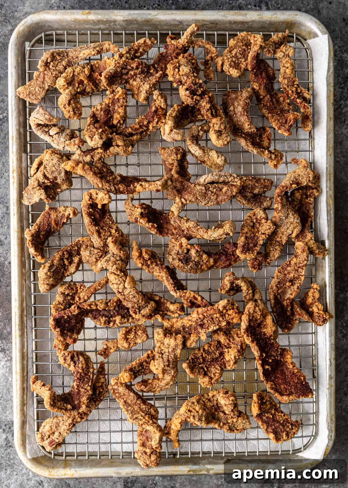 Sweet & Tangy Beijing Beef 5 Overhead view of thinly sliced beef strips, marinated and coated, resting on a wire rack above a baking sheet