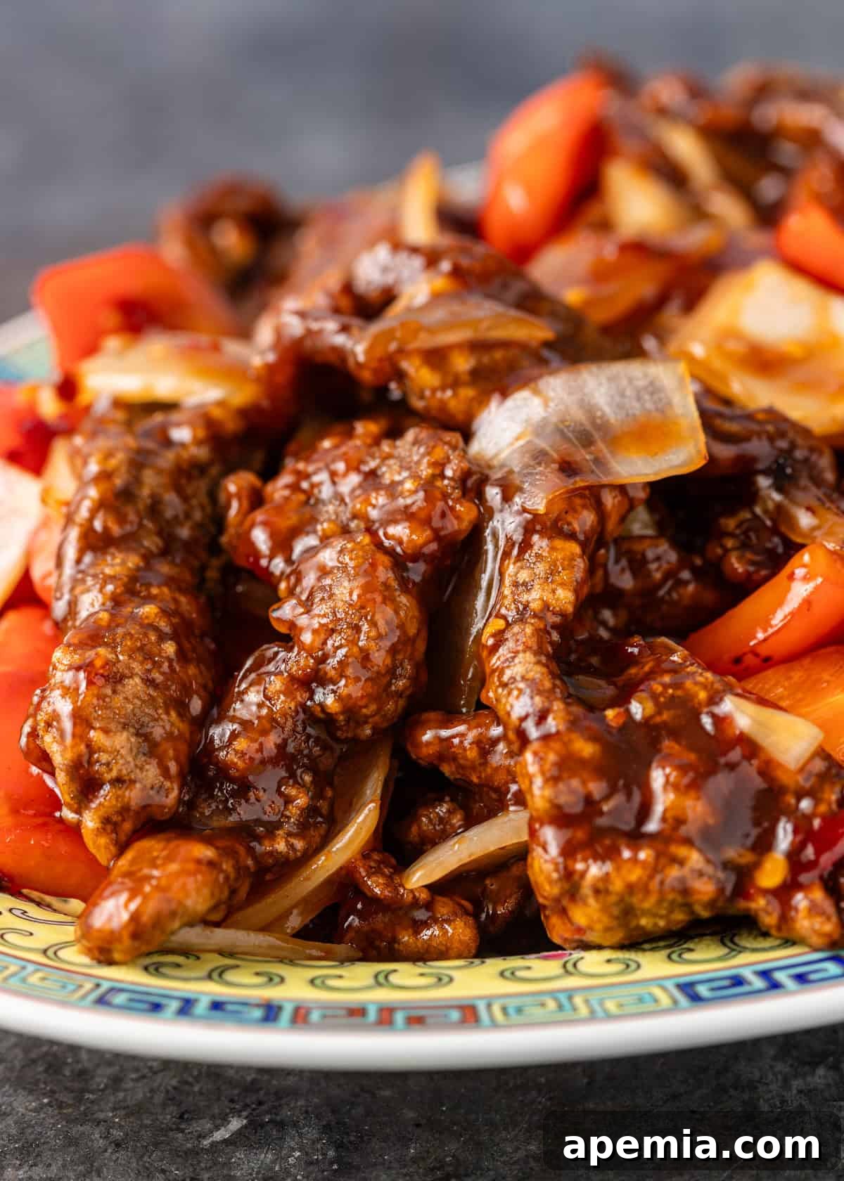 Sweet & Tangy Beijing Beef 8 Side view close-up of a serving of Beijing Beef, showing the glossy, thick sauce coating the crispy beef, bell peppers, and onions