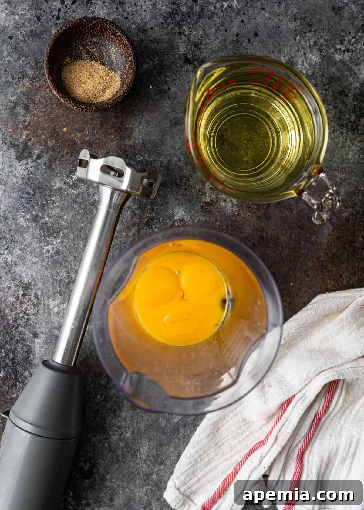 overhead: egg yolks in an immersion blender before blending with oil and celery salt to the side