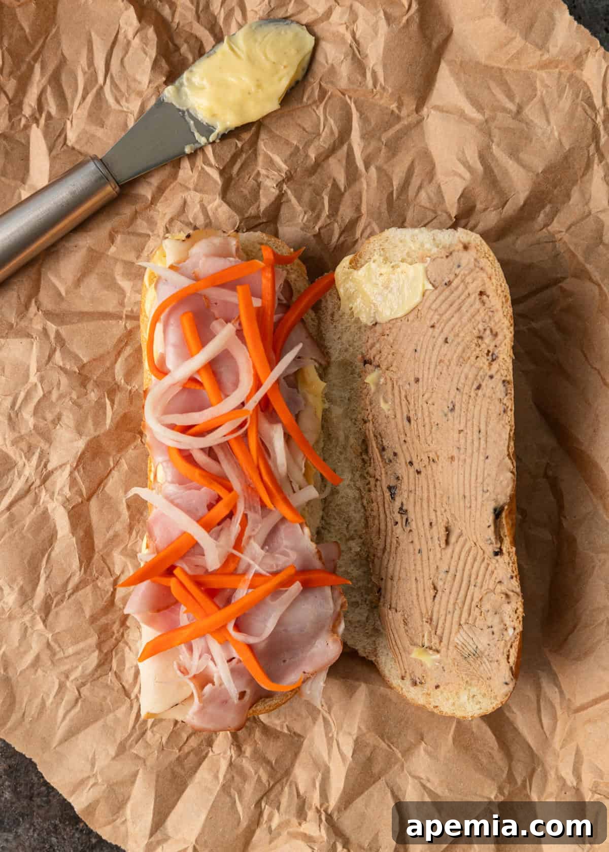 overhead: adding vietnamese mayo, paté, meat, and pickled veggies to an open baguette to make a banh mi