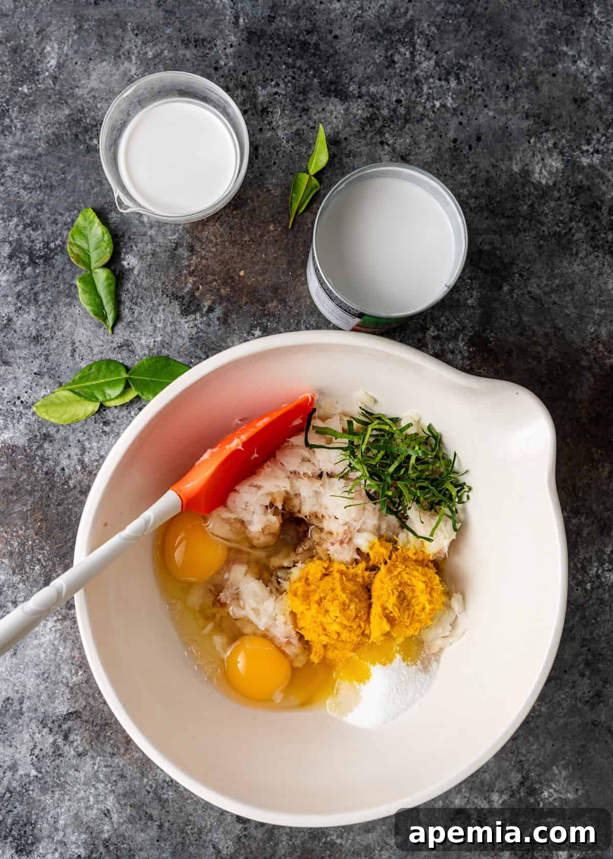 overhead process shot: ingredients for steamed fish curry in a large white mixing bowl