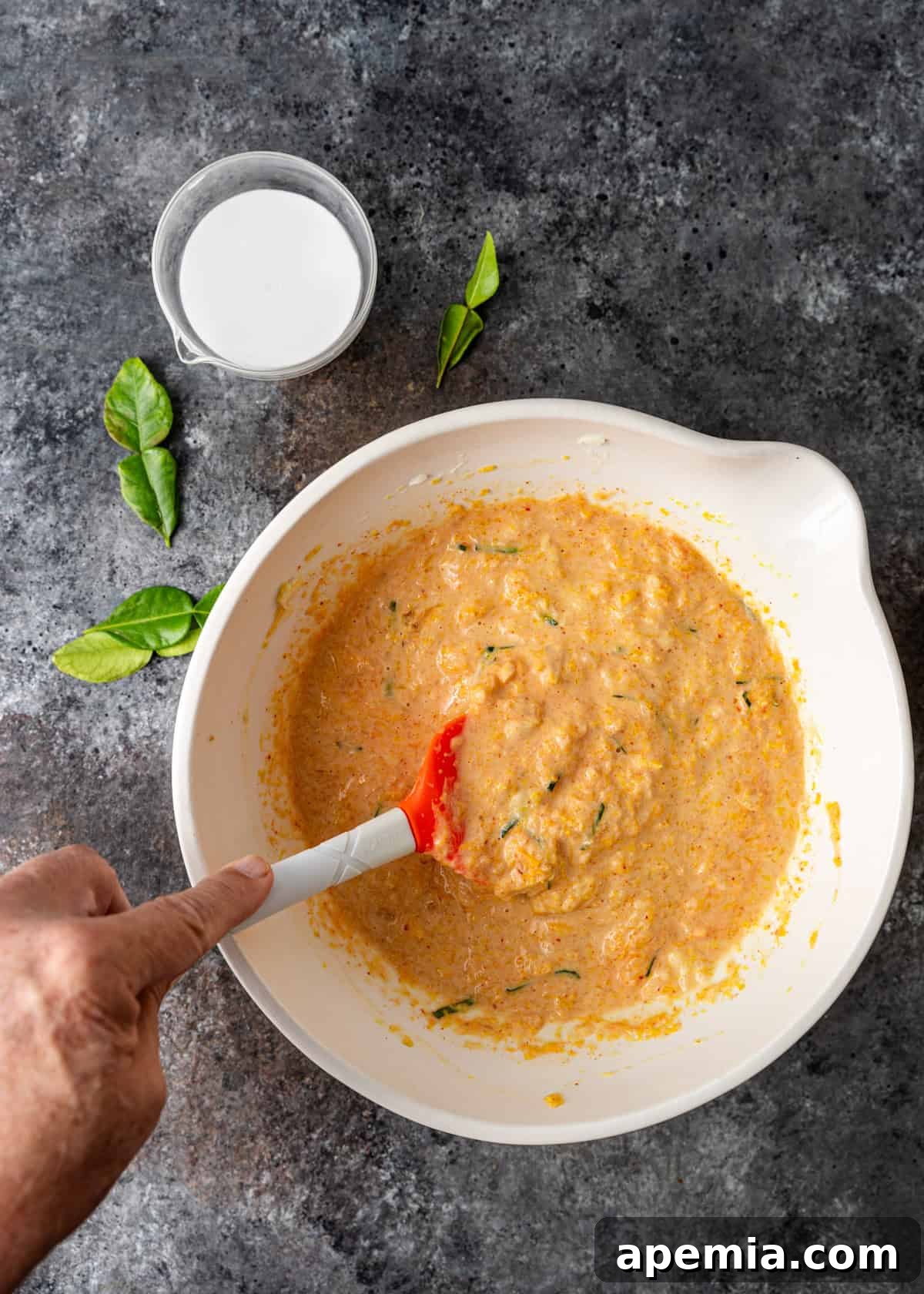 overhead process shot: mixing the ingredients for steamed fish curry in a large white mixing bowl