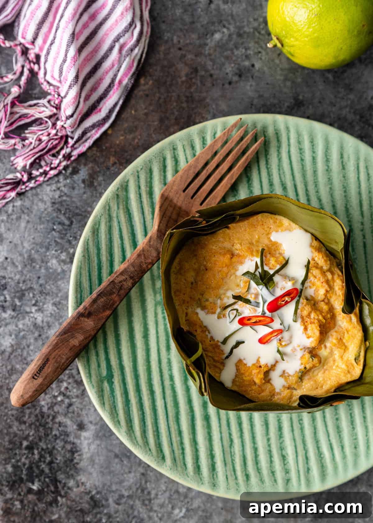 overhead: my amok recipe on a green plate with coconut milk and chiles on top with a wooden fork to the side