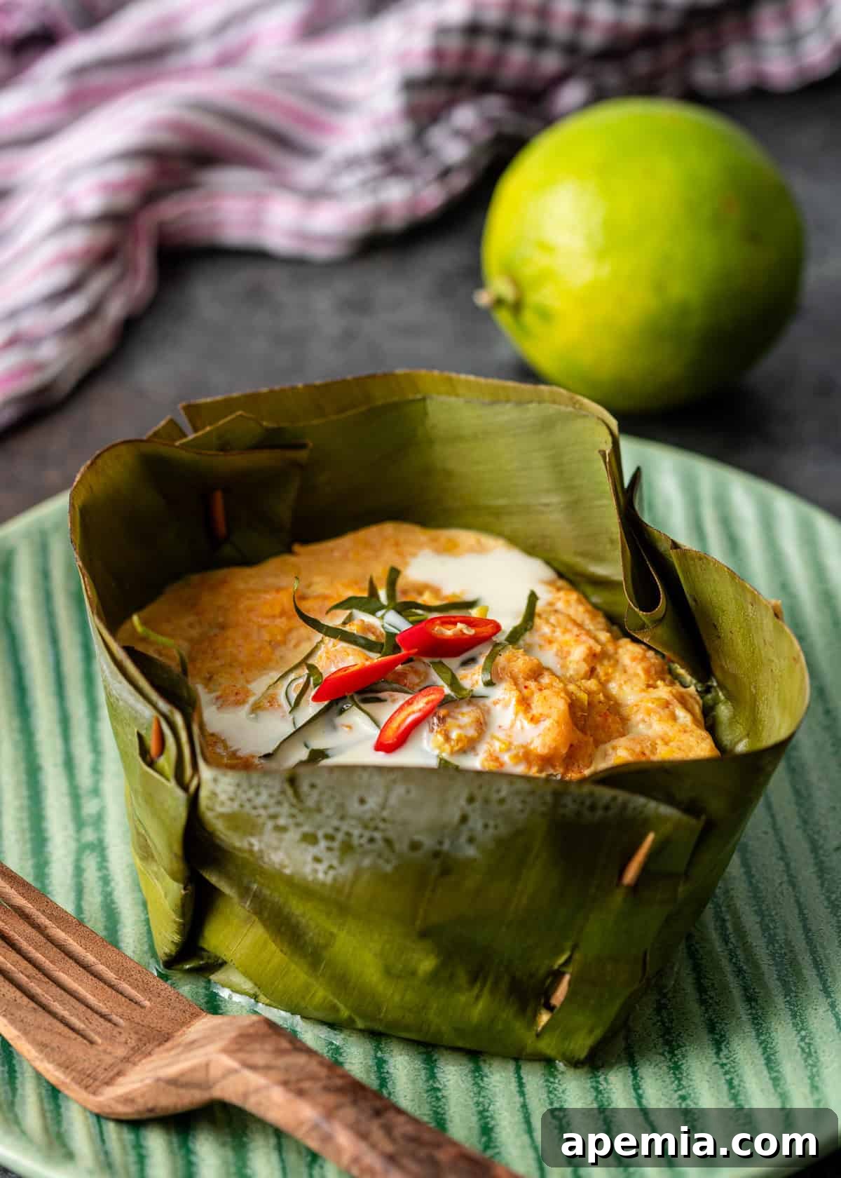 closeup: steamed fish curry in a banana leaf bowl with coconut milk and red chiles on top