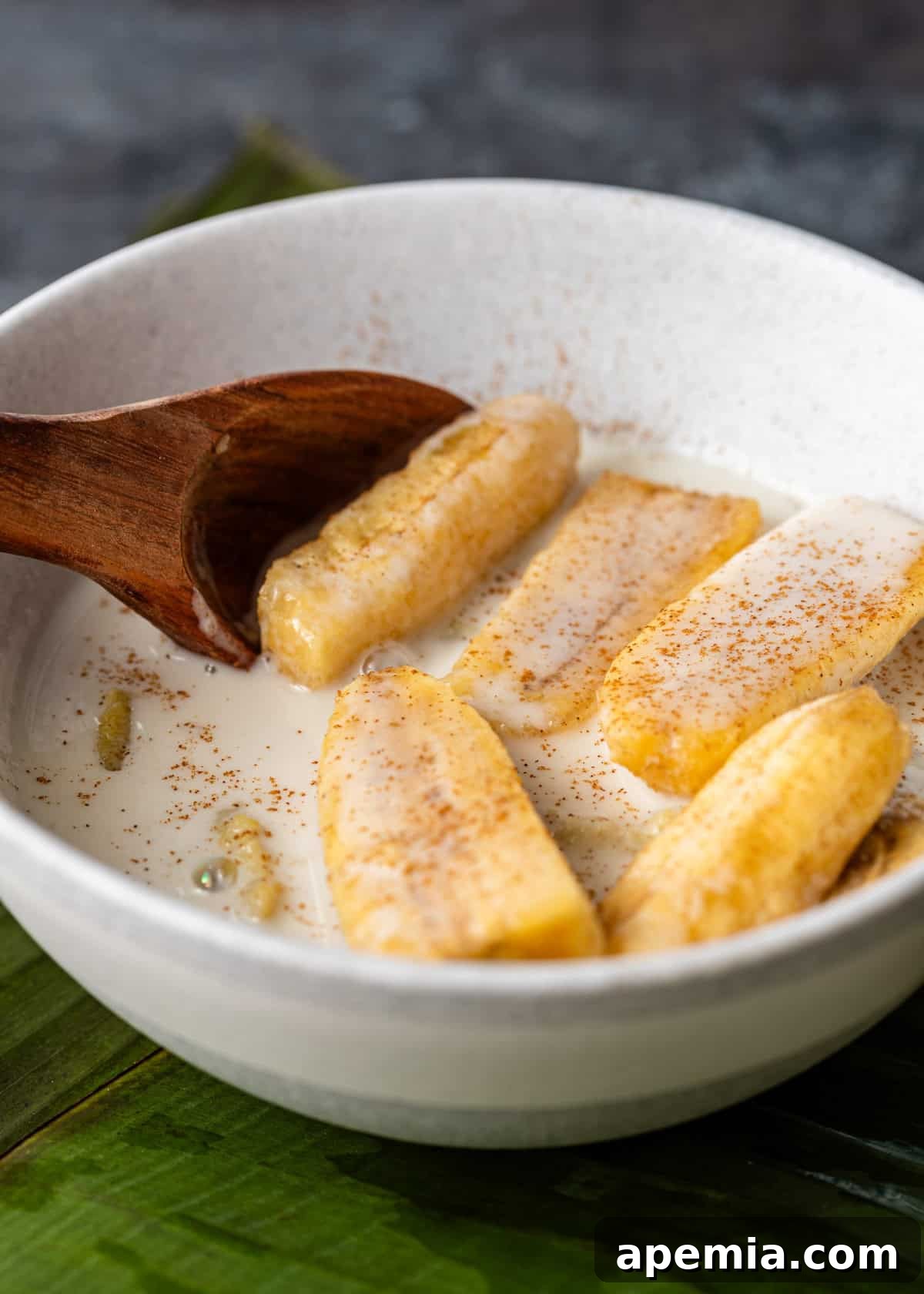 Close-up of Chak Ktiss (banana in coconut milk) served in a white bowl with a wooden spoon, highlighting the rich sauce and tender fruit.