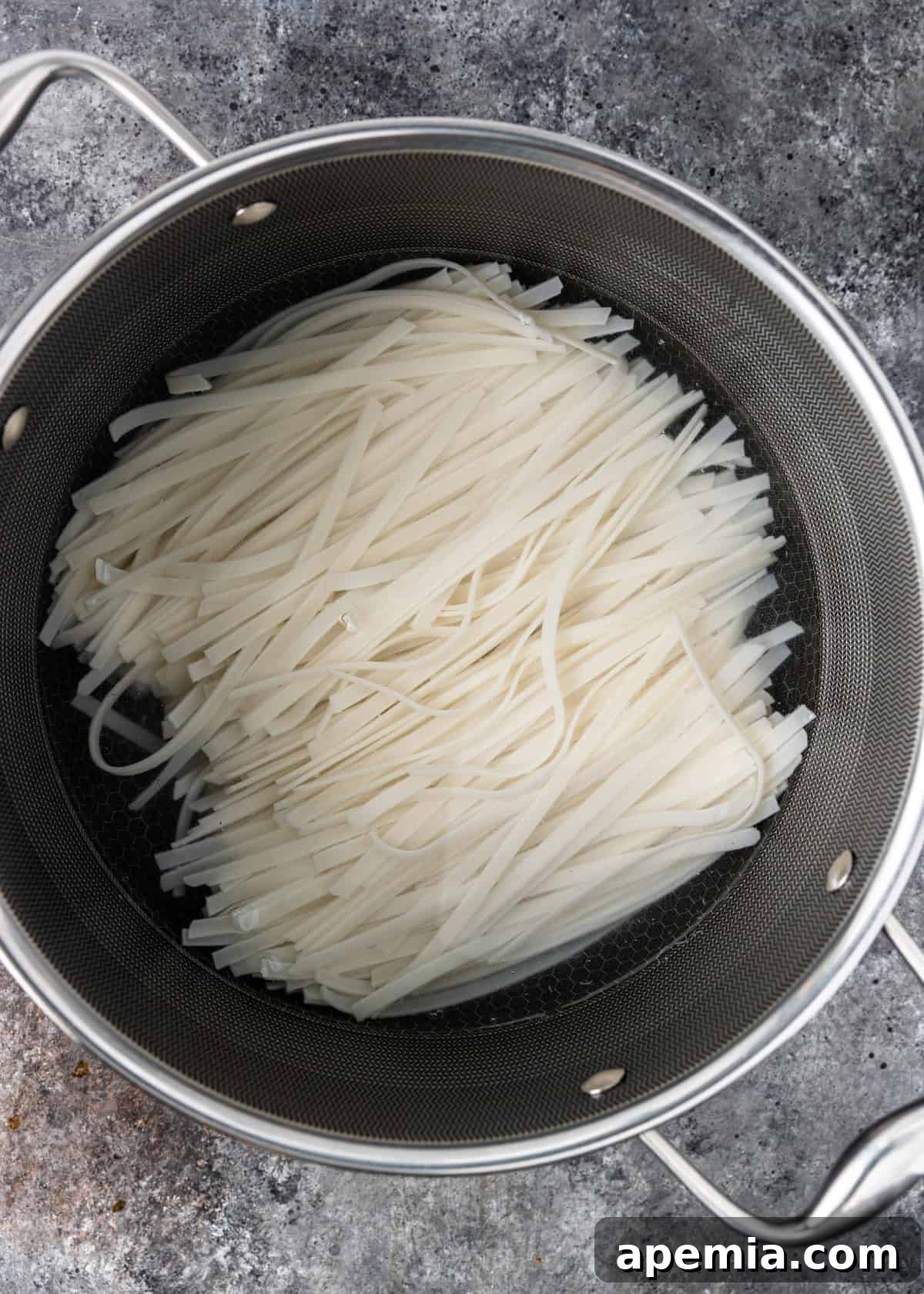 Bold and Spicy Thai Basil Noodles 4 Overhead process shot demonstrating how to soak wide rice noodles in hot water until pliable for Drunken Noodles.