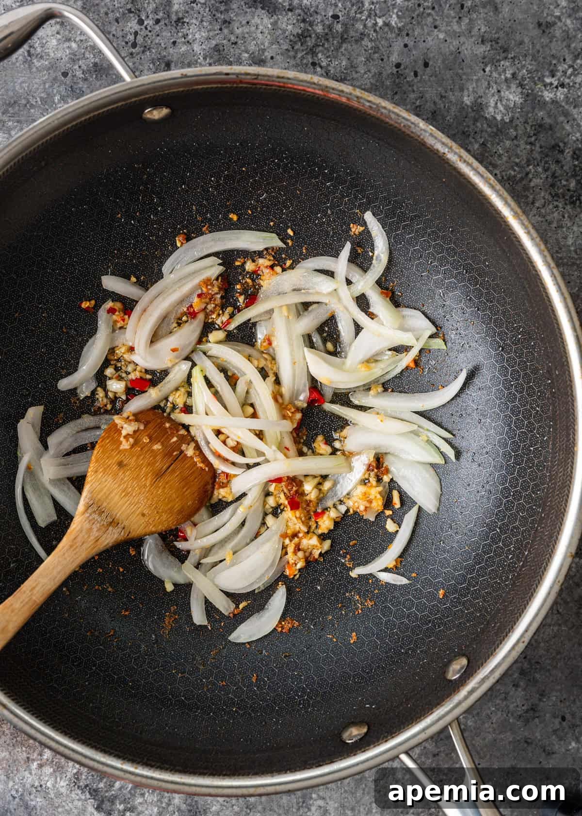 Bold and Spicy Thai Basil Noodles 6 Overhead process shot showing sliced onions and other seasonings being sautéed in a hot wok, releasing their fragrant aromas.
