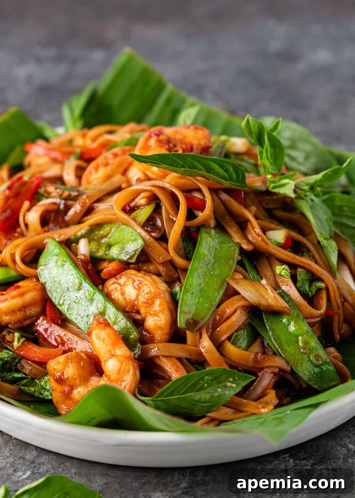 Bold and Spicy Thai Basil Noodles 9 Closeup of a bowl of Drunken Noodles (Pad Kee Mao) featuring plump shrimp, bright green snow peas, and vibrant Thai basil, drenched in the savory sauce.
