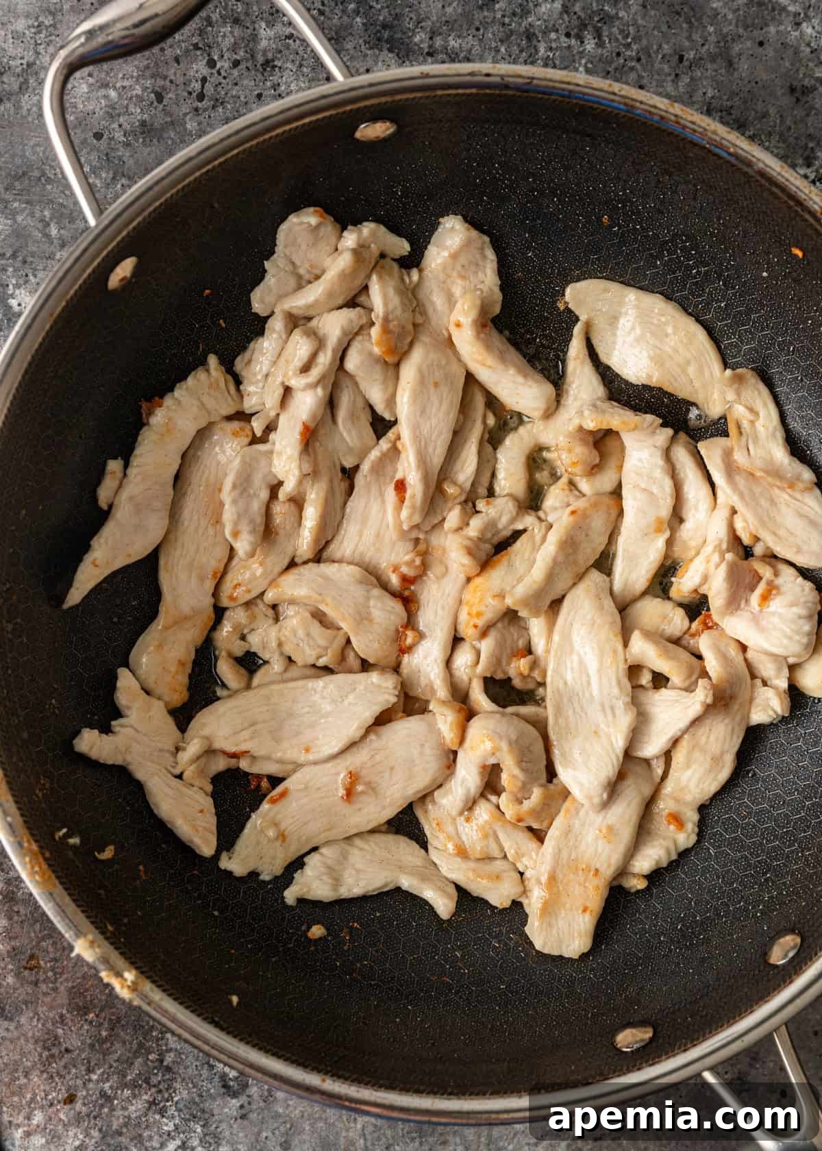 Process shot: Marinated chicken being expertly stir-fried in a hot wok, showing early stages of cooking as it begins to brown and crisp.