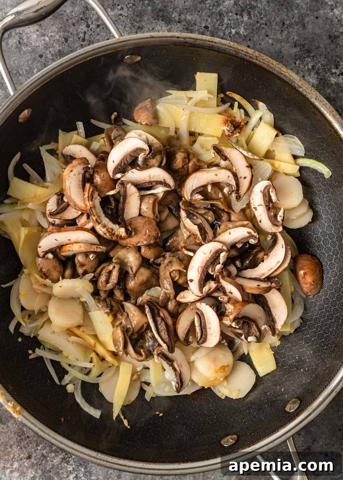 Process shot: Freshly chopped vegetables including mushrooms, bamboo shoots, and water chestnuts being added to the partially cooked chicken in the wok, illustrating the stir-fry sequence.