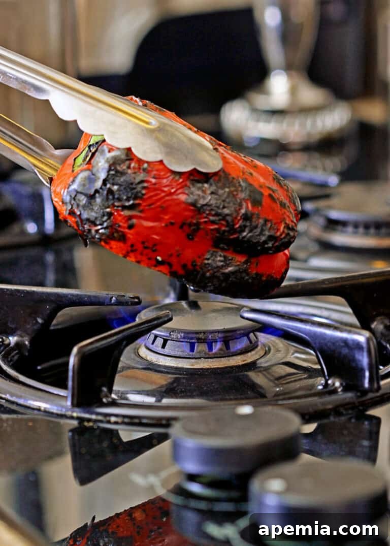 Red bell pepper being charred over an open flame on a stovetop, essential for a smoky harissa.