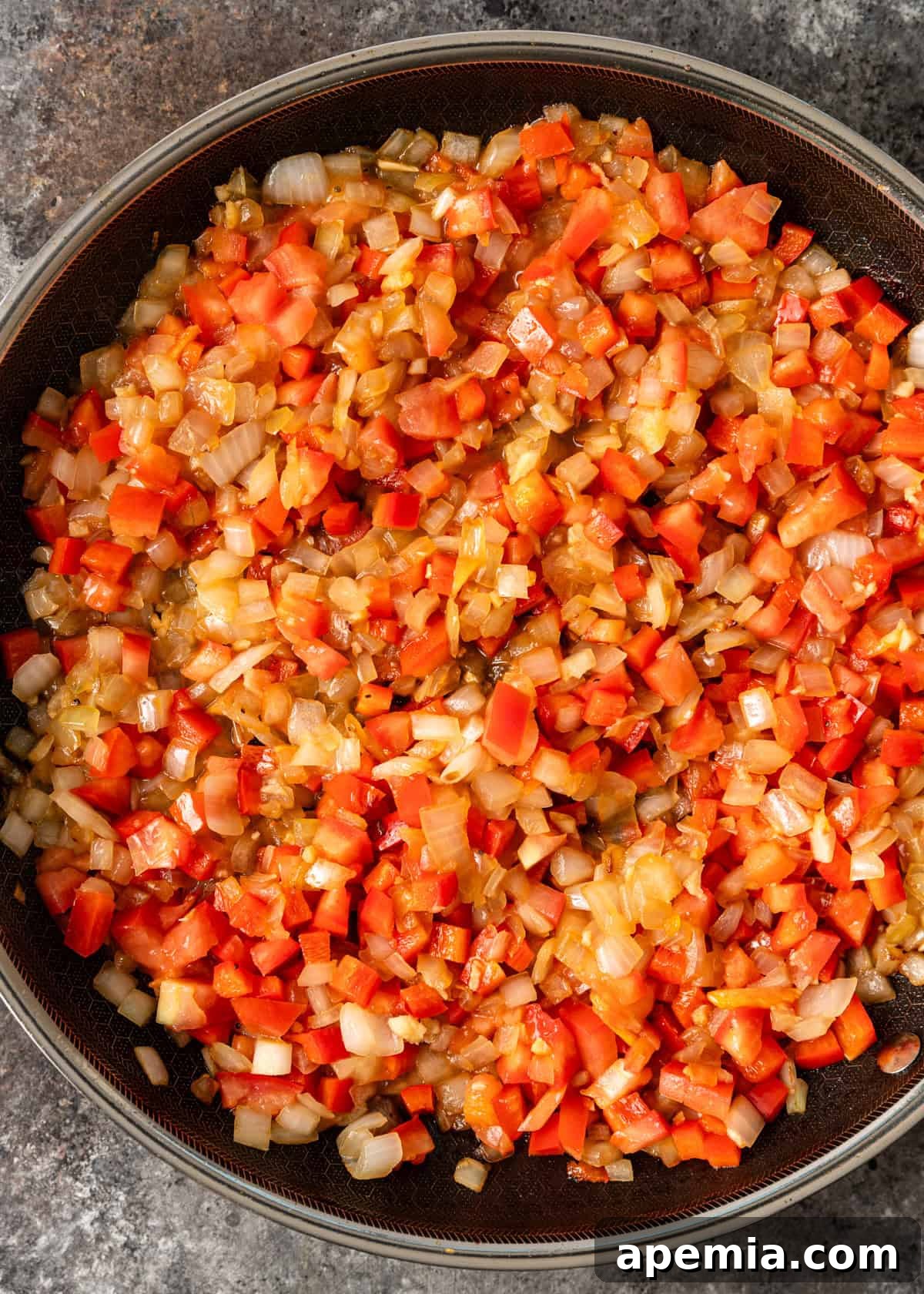 Creamy Hungarian Chicken Delight 7 overhead process shot: onion, garlic, tomatoes, and red bell pepper cooking in a skillet