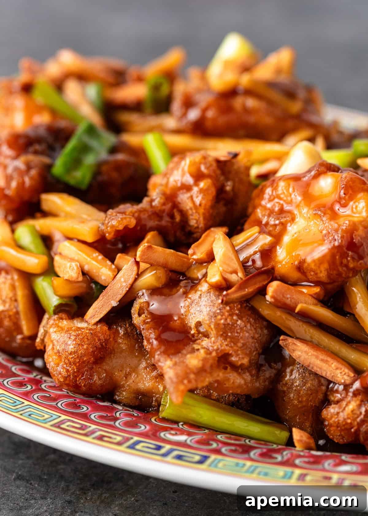 Closeup of almond chicken on a plate with sauce, slivered almonds, shredded carrots, and bamboo shoots