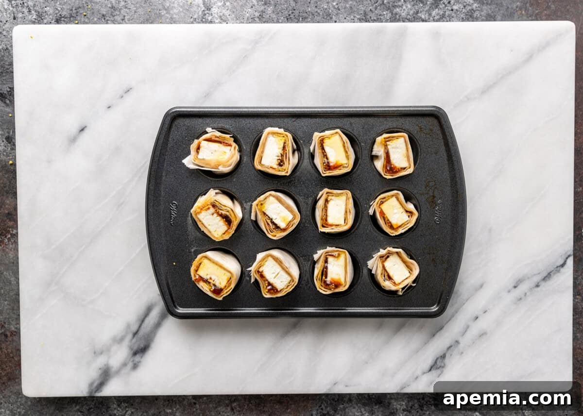 Overhead process shot: Transferring the feta in filo rounds to a prepared mini muffin tin before baking.