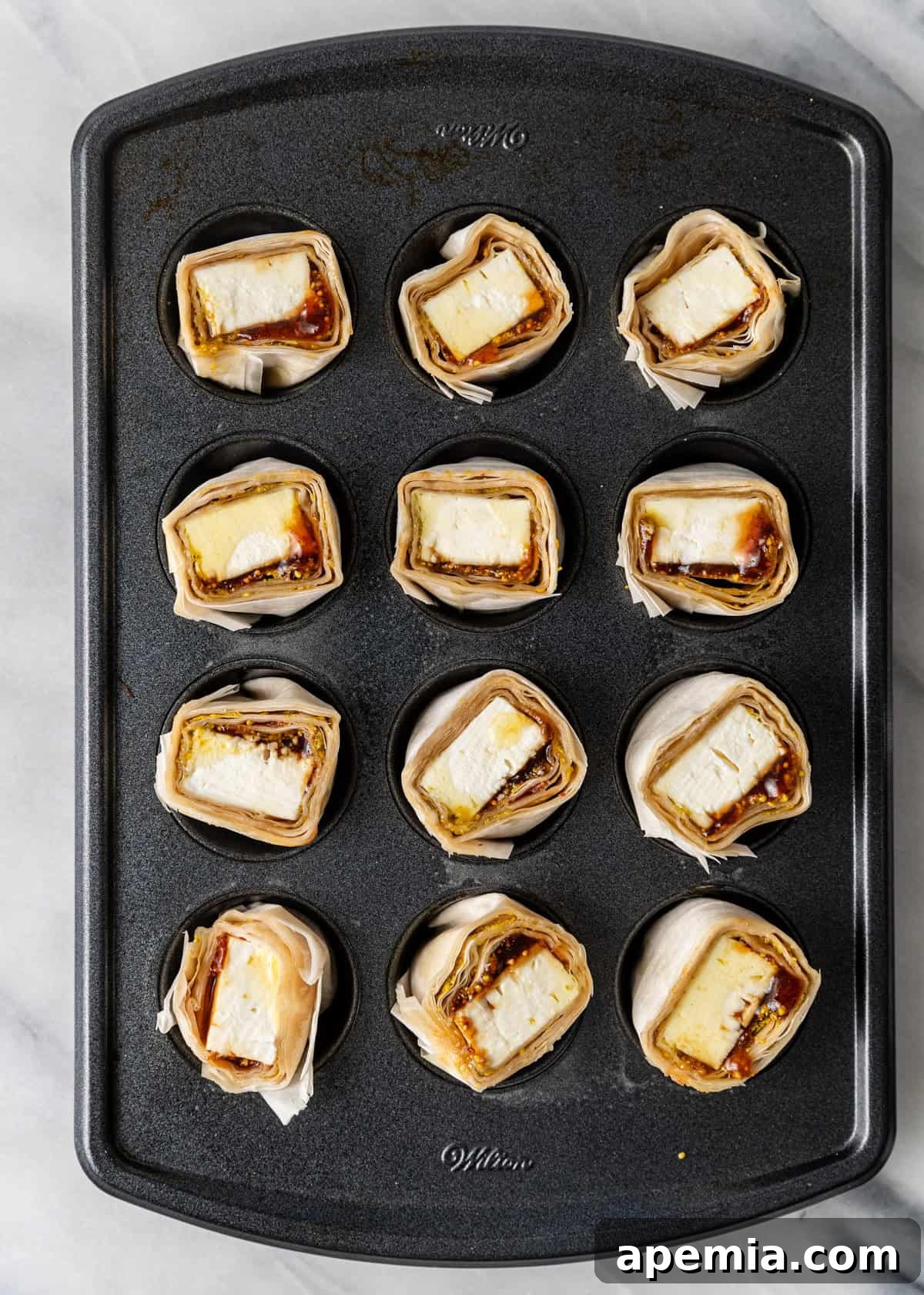 Overhead view of feta in filo rounds perfectly placed in a mini muffin tin, ready to be baked to golden perfection.