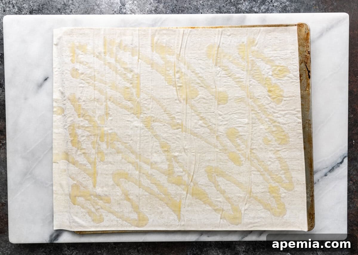 Overhead process shot: Drizzling a generous amount of olive oil over layered sheets of filo dough.