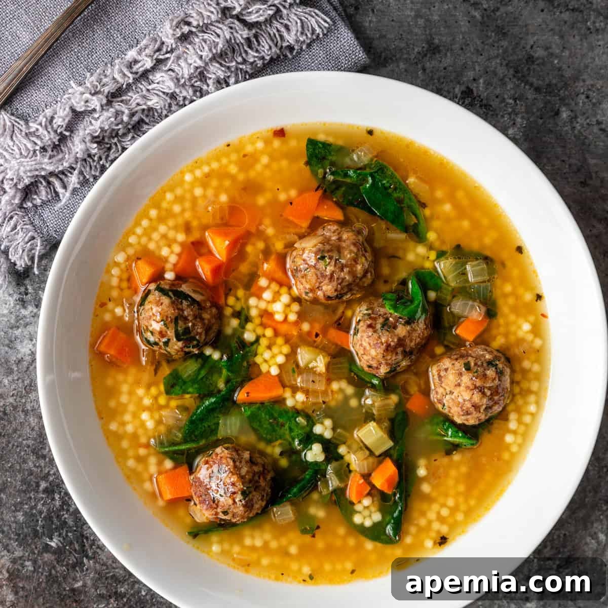 overhead: a bowl of Italian wedding soup with meatballs, spinach, and pasta
