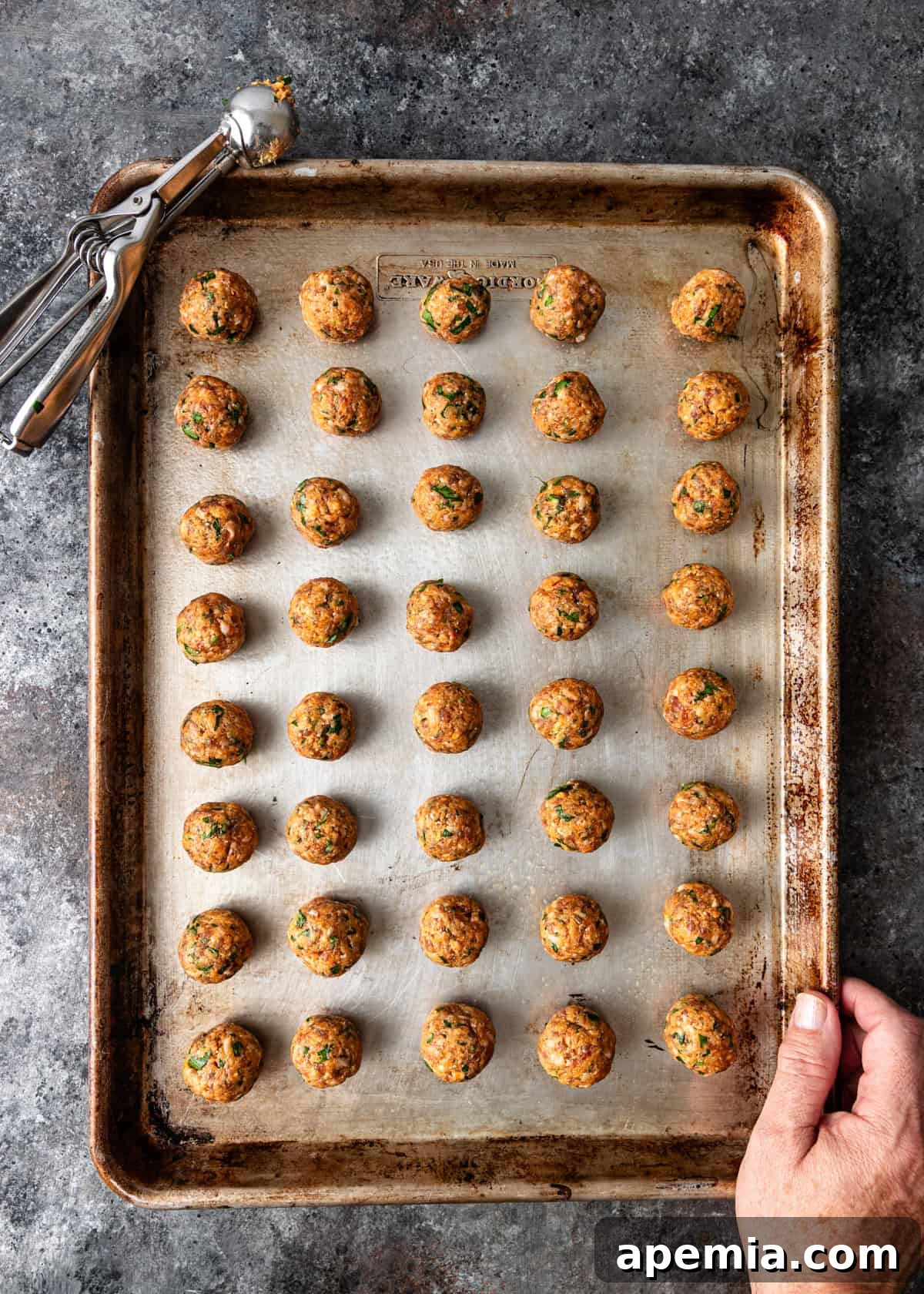 overhead process shot: raw meatballs rolled and ready to bake on a baking sheet