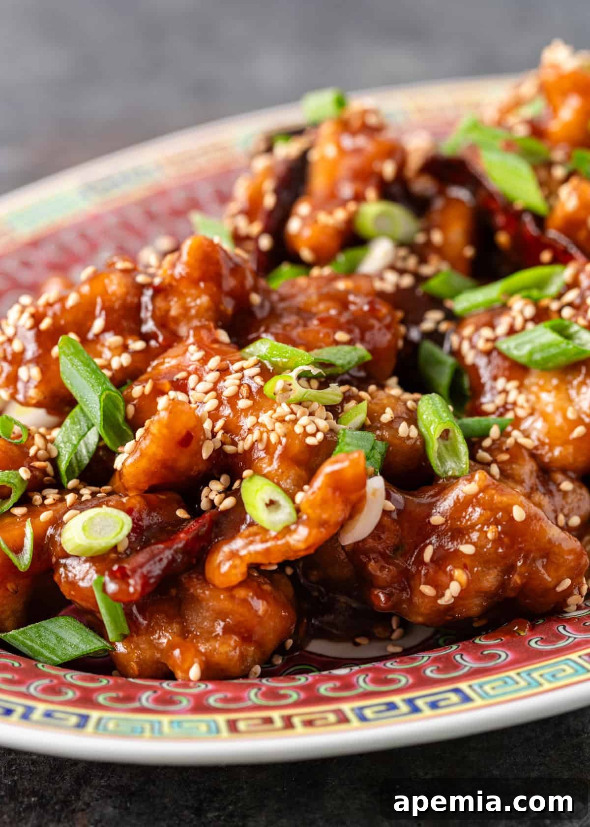 Closeup: General Tso's chicken topped with a generous sprinkle of sesame seeds and freshly sliced green onions, showcasing the vibrant colors and sticky sauce.