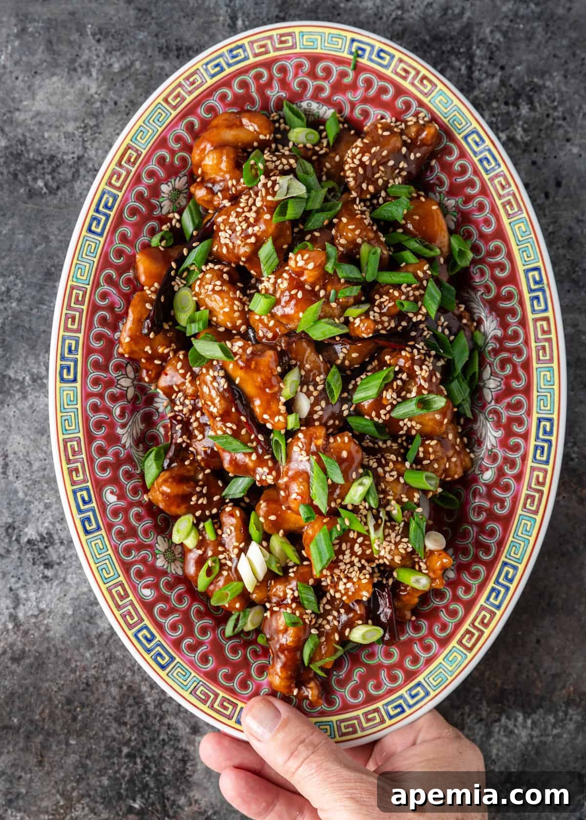 Overhead shot: a large serving platter brimming with my General Tso's chicken recipe, glistening with sauce and topped with fresh garnishes.