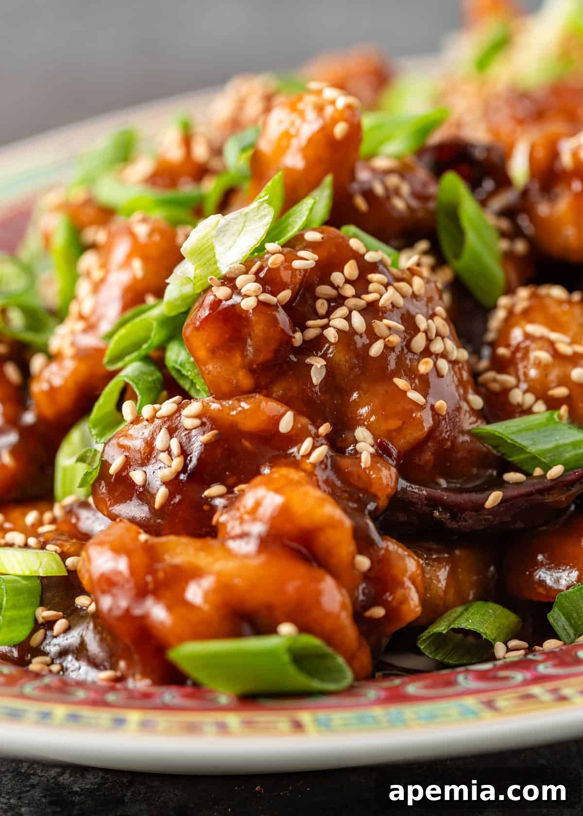 Extreme closeup: my General Tso's chicken recipe garnished beautifully with sesame seeds and fresh green onion, showcasing the enticing texture and vibrant sauce.