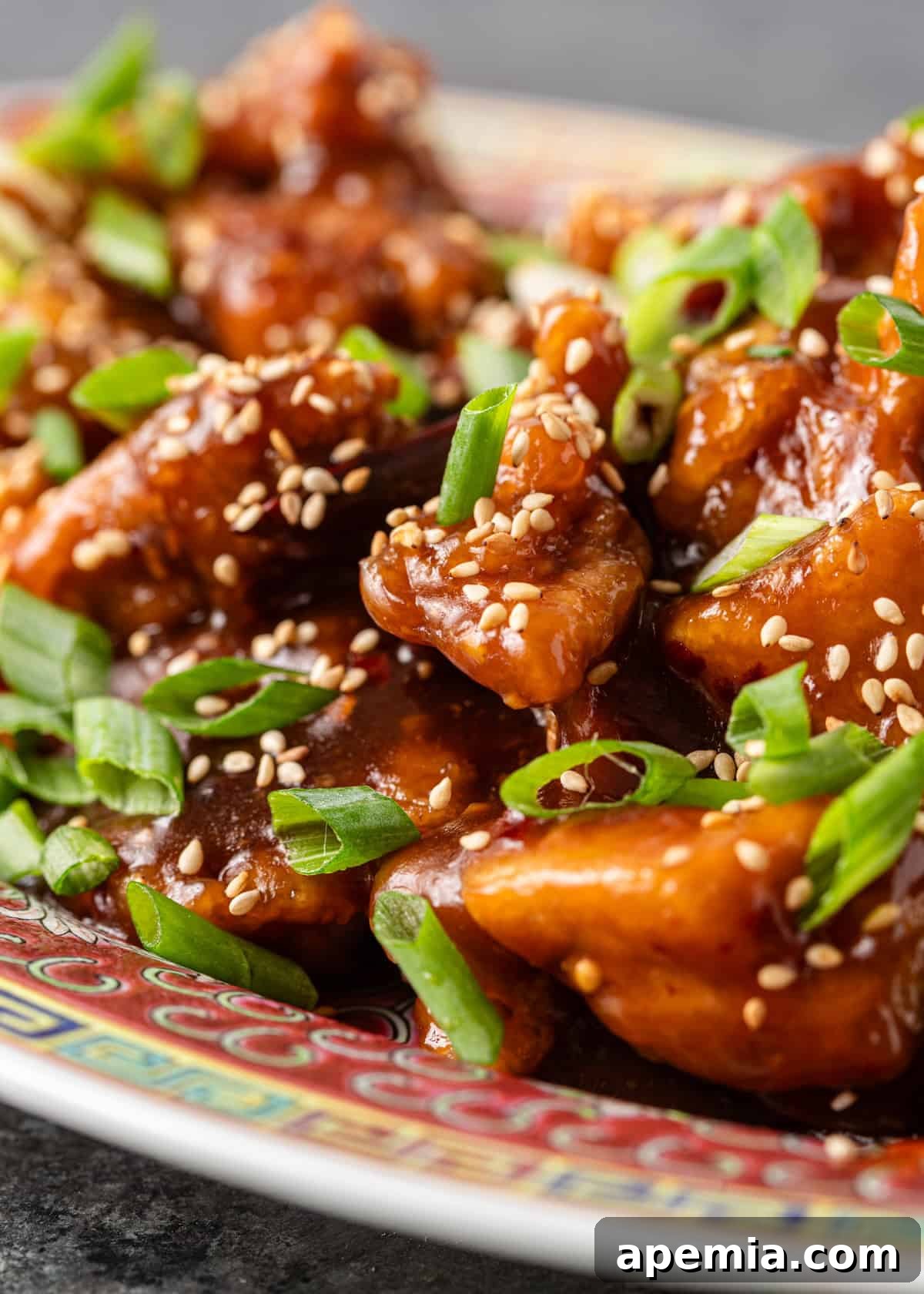 Closeup: General Tso's chicken generously covered in the signature sauce, adorned with toasted sesame seeds and fresh sliced green onions, ready to be devoured.