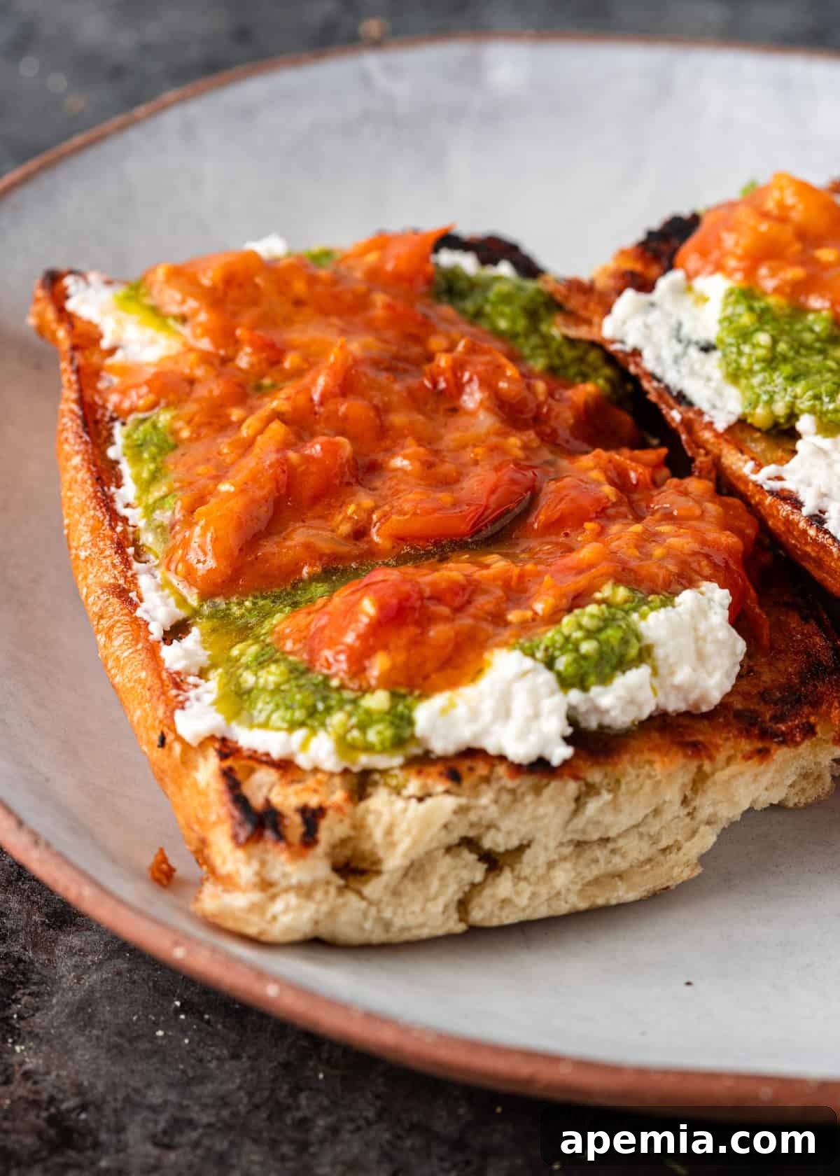 Closeup shot: toasted bread with creamy cheese, fresh pesto, and vibrant tomato garlic confit. An appealing appetizer.