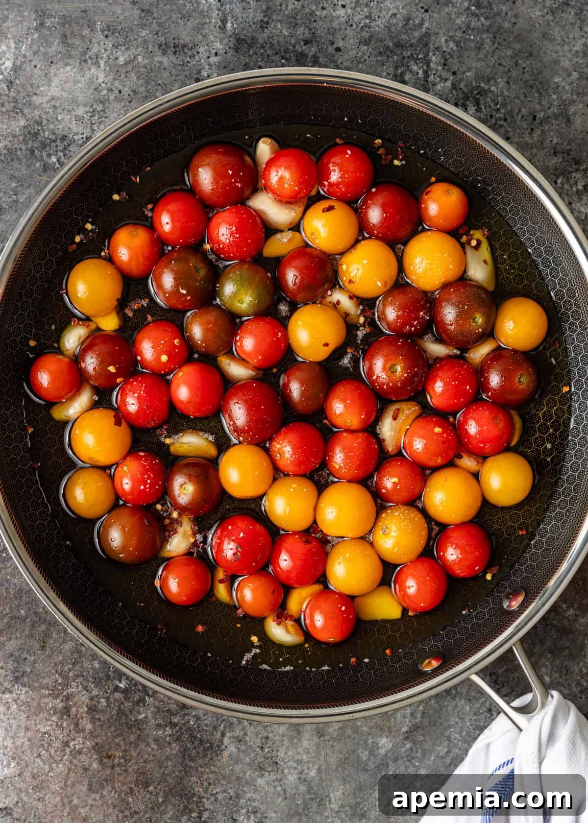Overhead process shot: cherry tomatoes in a skillet with oil and garlic before cooking on the stovetop.