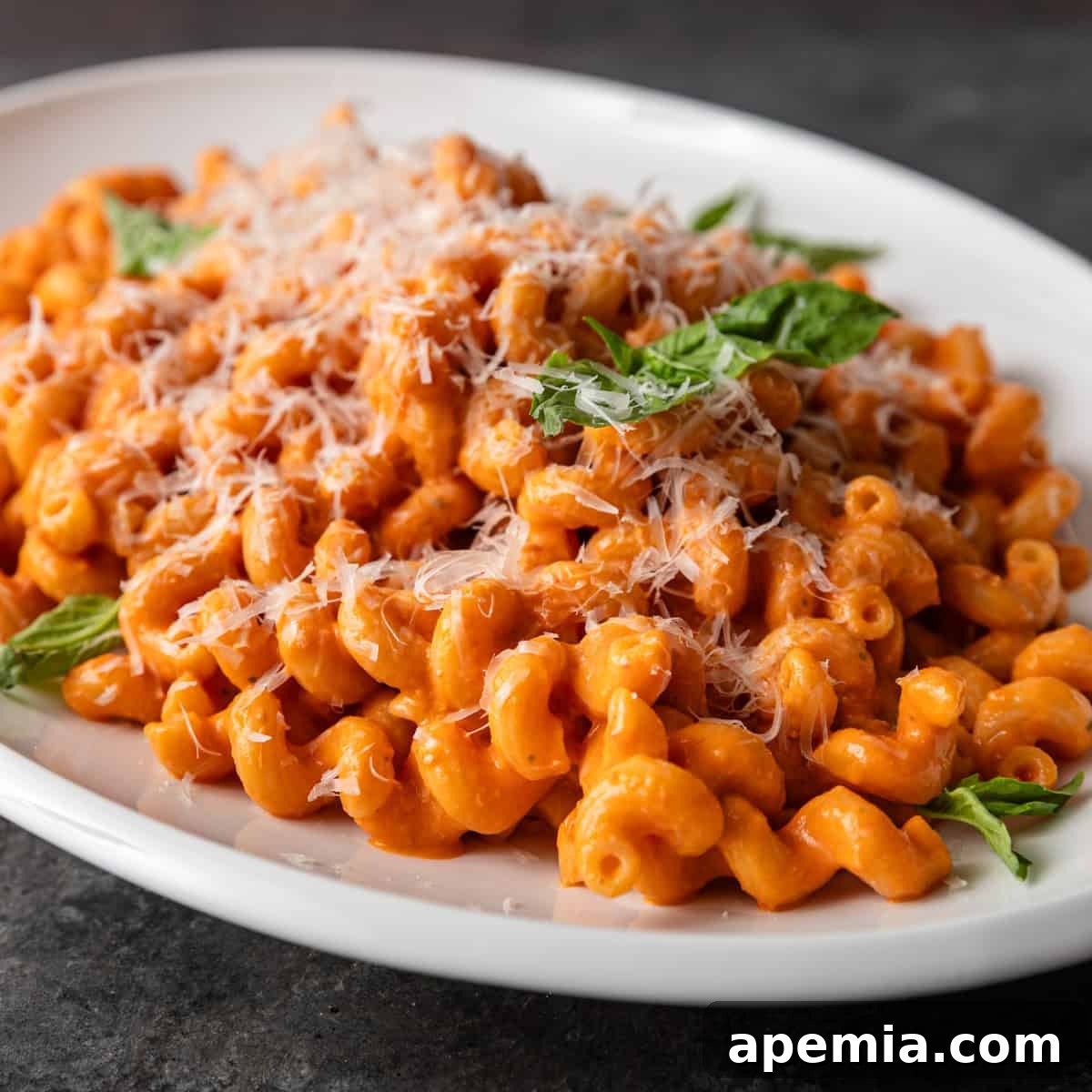 Closeup of creamy tomato confit pasta, garnished with fresh parmesan and vibrant basil leaves