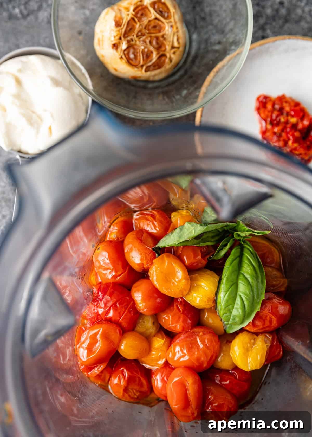 Overhead process shot showing tomato confit sauce in a blender before blending, highlighting the whole roasted ingredients